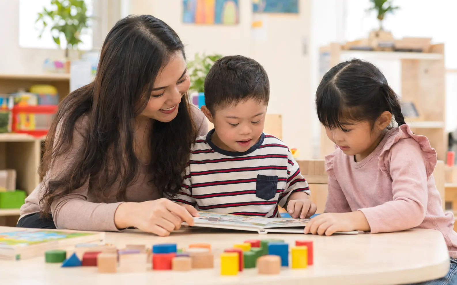 A child with Down syndrome reading with an educator and a classmate